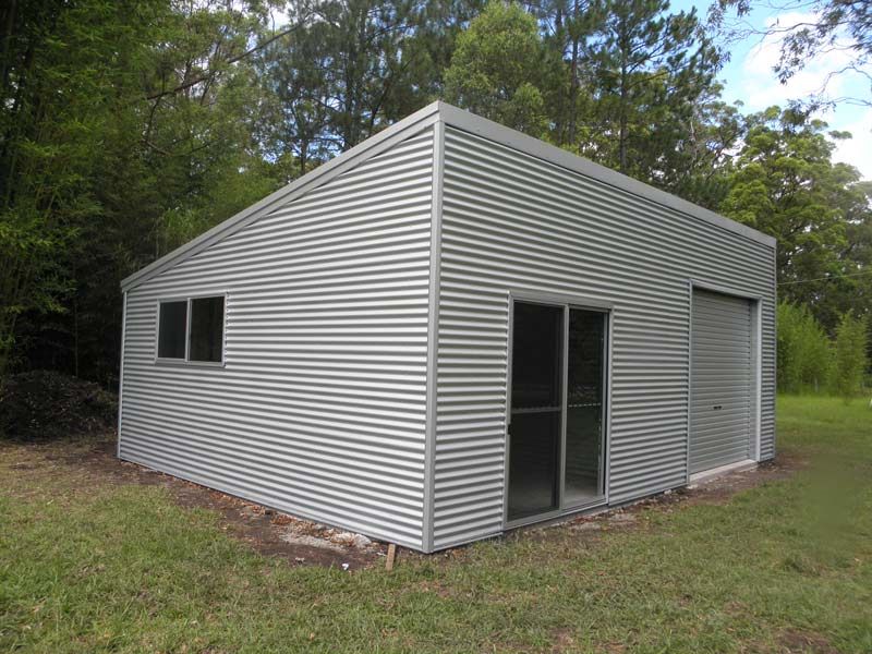 A Small Metal Building With A Sliding Glass Door Is Sitting In The Middle Of A Grassy Field