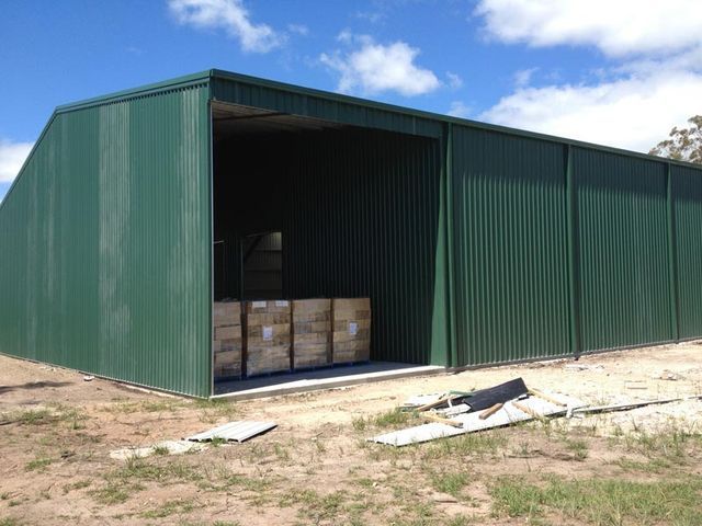 A Green Metal Building With Boxes In The Doorway – South Kempsey NSW - Fair Dinkum Builds Macleay Valley Sheds