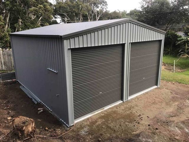 A Gray Garage With Two Roller Doors Is Sitting On Top Of A Dirt Field 