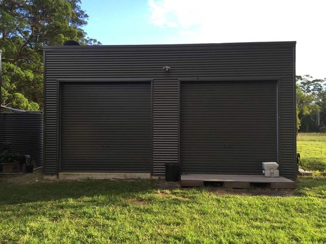 A Black Garage With Two Garage Doors Is Sitting On Top Of A Lush Green Field 
