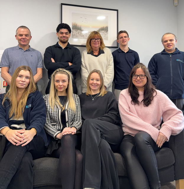 Group portrait of eight colleagues in an office, seated and standing on a sofa, smiling at the camera.