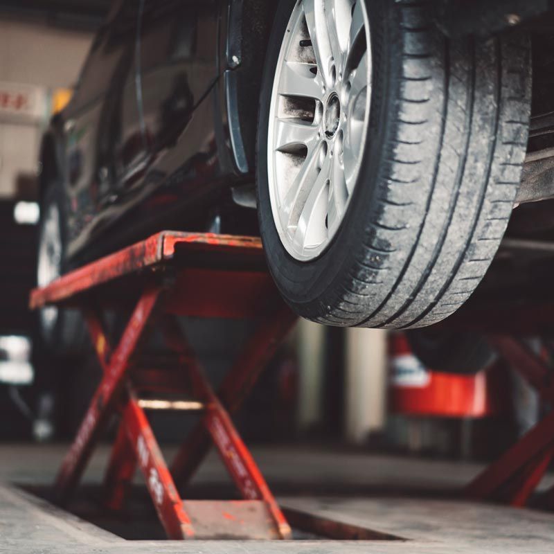 Car lifted on a red hydraulic jack in an auto repair shop, with a tire visible in the foreground