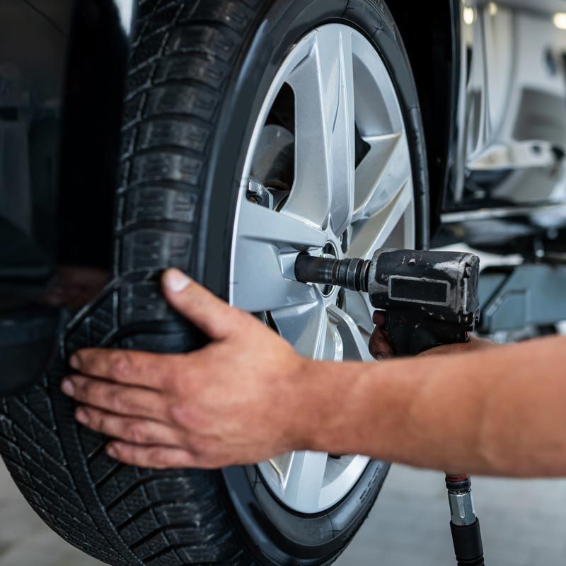 Mechanic using an impact wrench to tighten a car tire on a silver wheel
