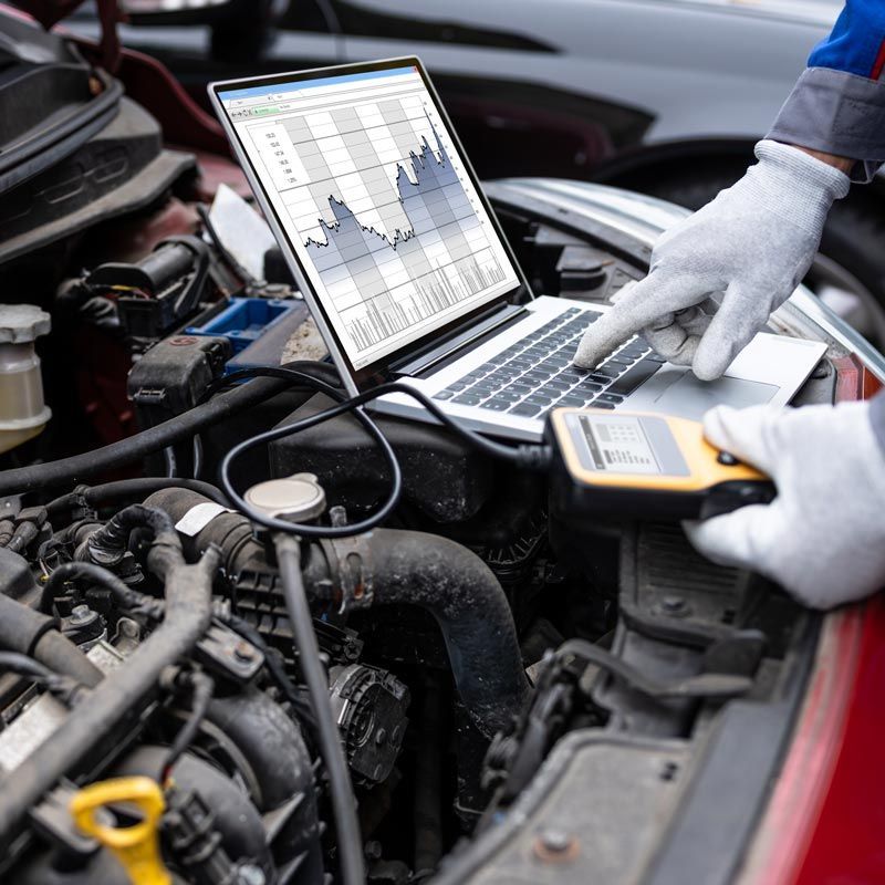 Mechanic using laptop and diagnostic tool on a car engine in a garage
