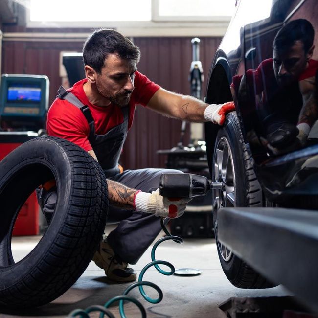 Mechanic inflating a car tire in a garage beside a black vehicle