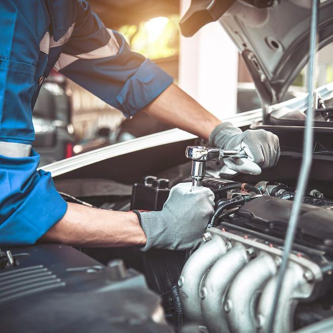 Mechanic in blue uniform repairing a car engine under the hood