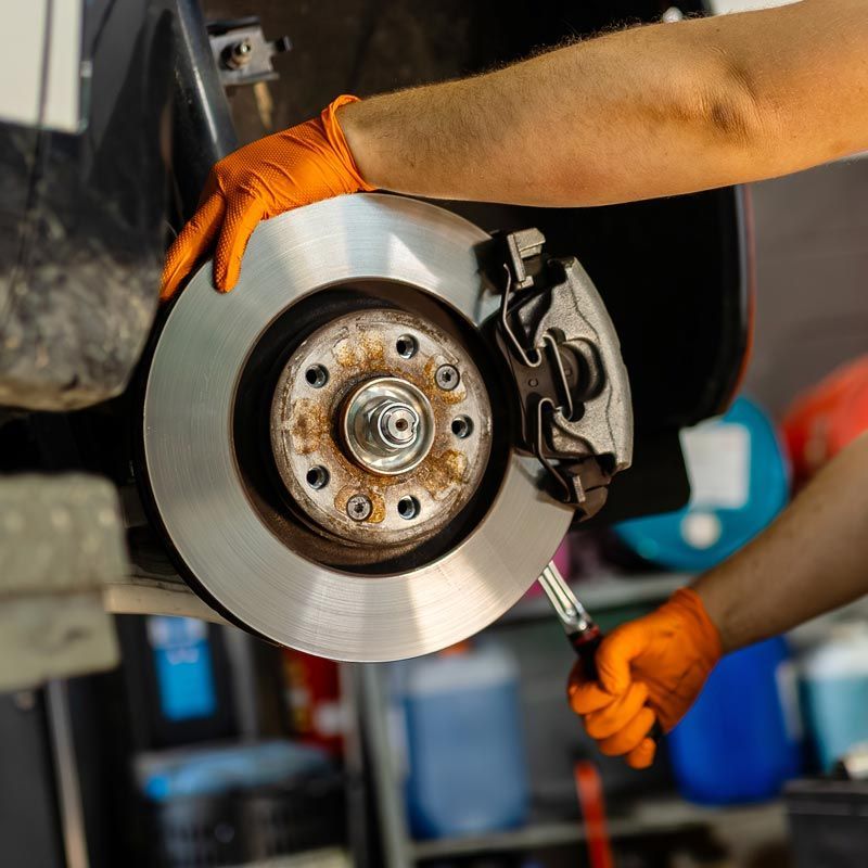 Mechanic in orange gloves replacing a car brake rotor in a garage