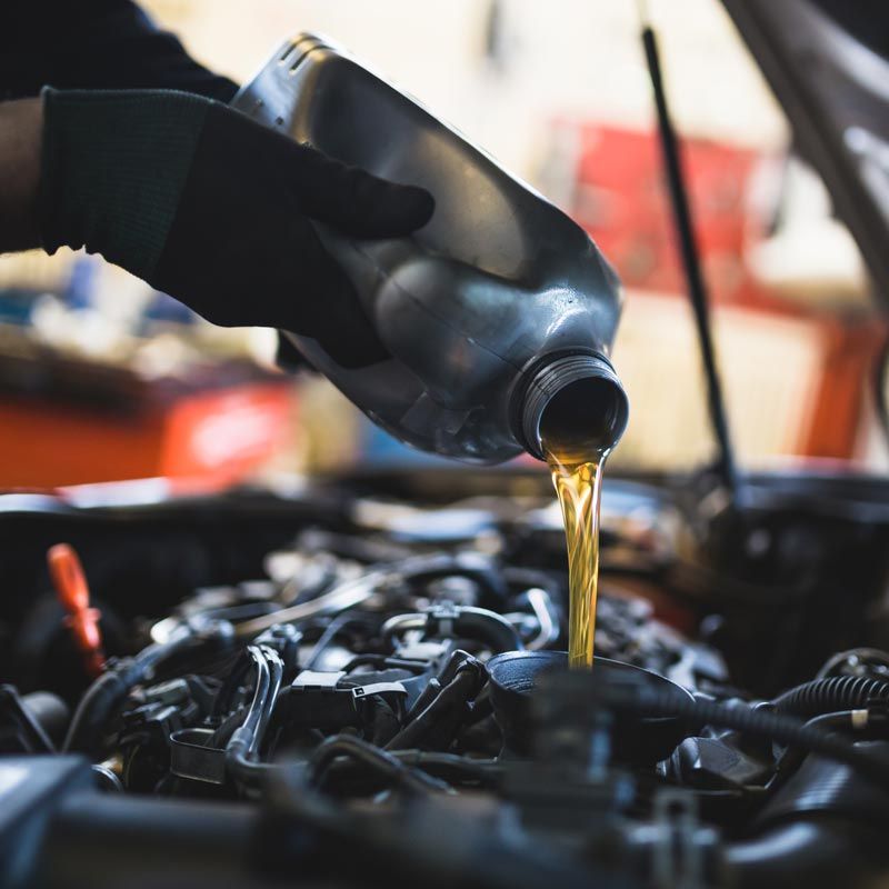 Mechanic pouring motor oil from a black bottle into an engine bay