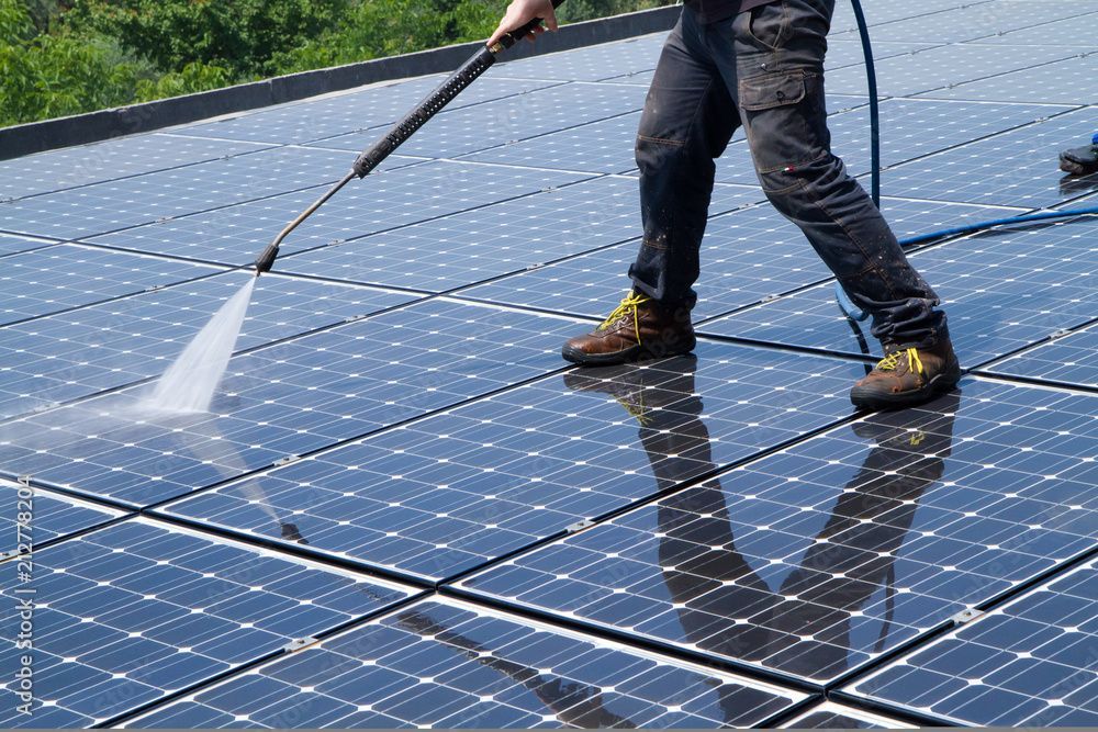 A man is cleaning a solar panel with a high pressure washer.