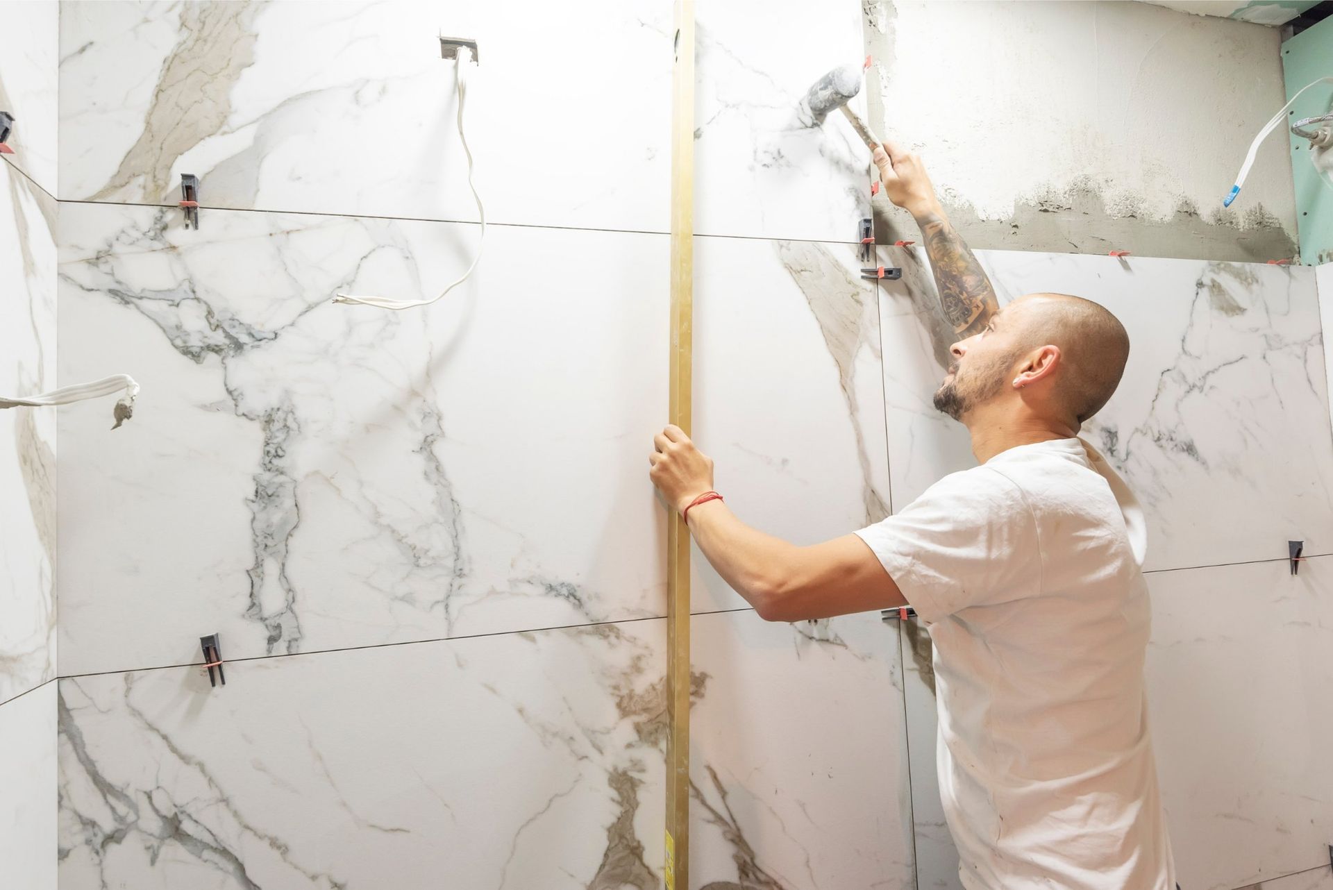 Man tiling a wall, using a hammer and level. White and grey tiles.