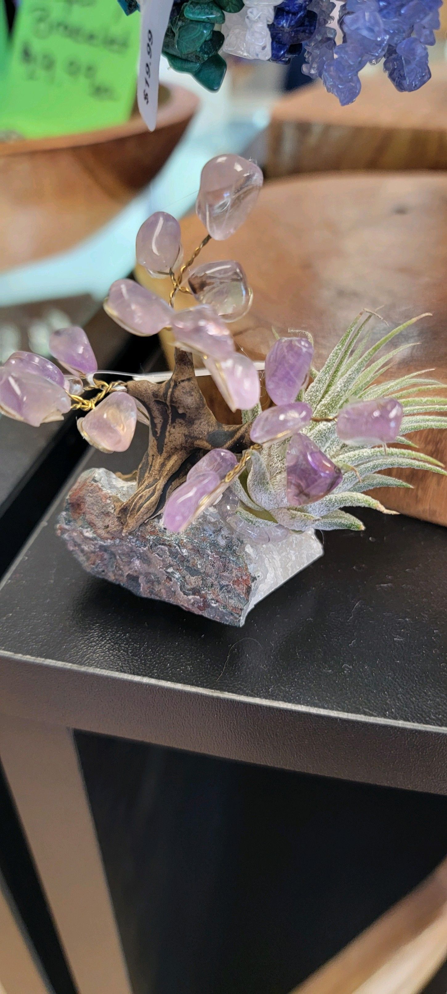 Small tree sculpture made of purple crystal with a stone base, on a dark surface.