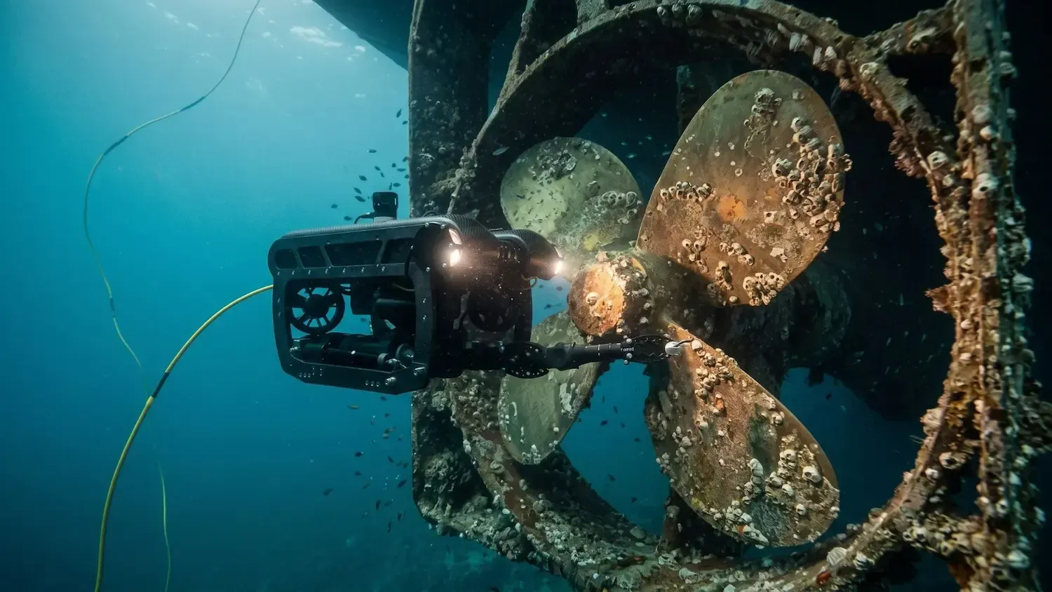 Underwater diver beside a blue-lit robotic device on a rocky seabed
