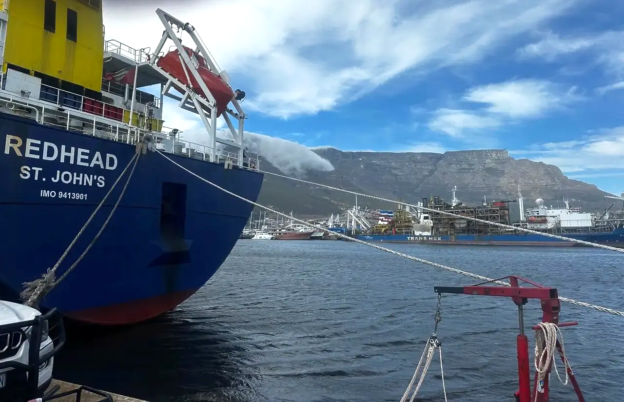 Red cargo ship in harbor with misty hills and blue sky beyond the water