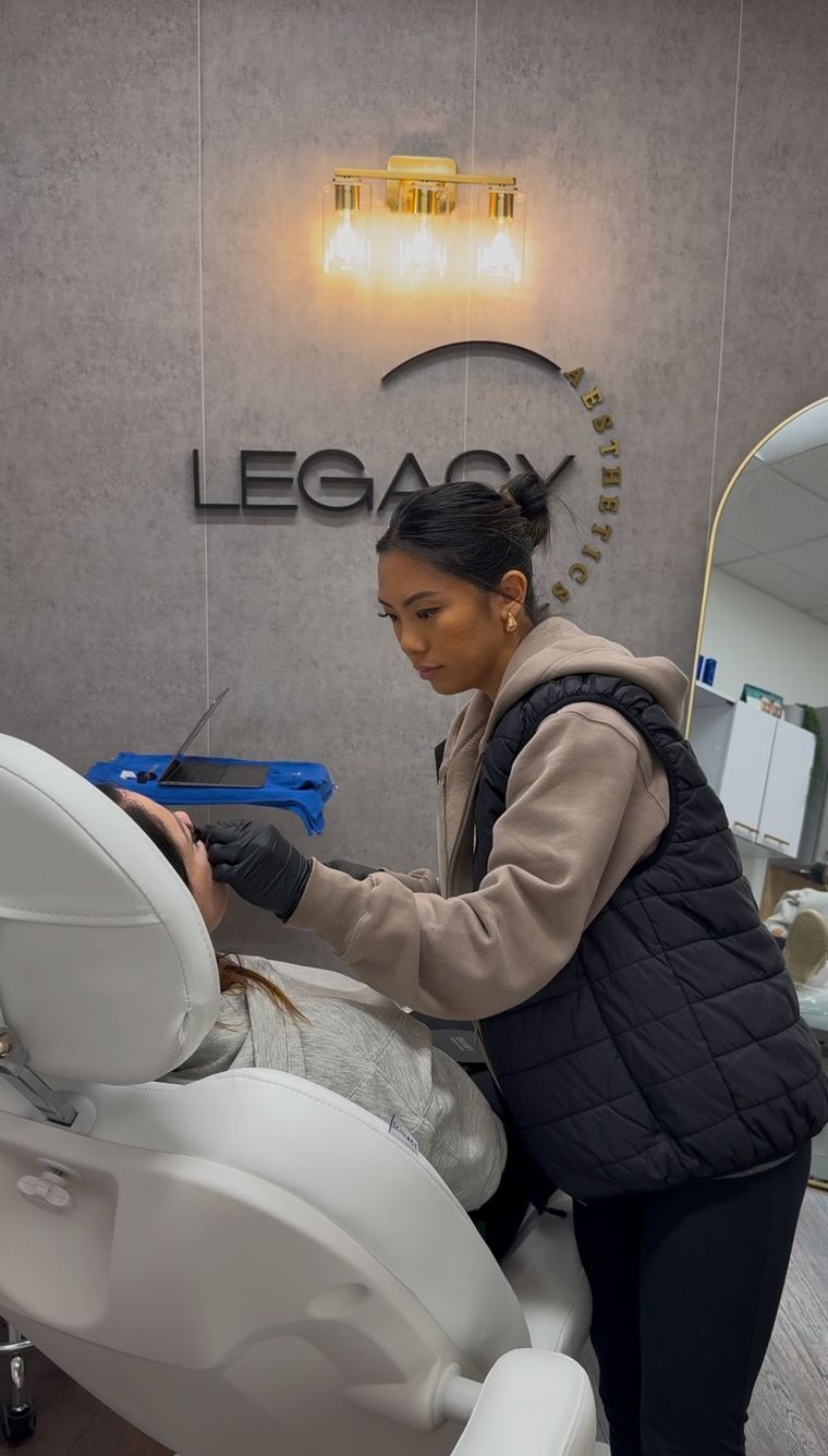 Person cleaning a white salon chair in a modern salon with “LEGACY” sign on the wall.