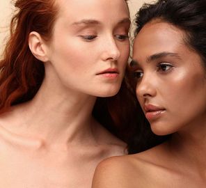 Two women in a close-up portrait, facing each other with soft expressions against a neutral background