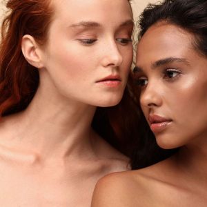 Two women in close-up, one with red hair, softly facing each other against a warm background