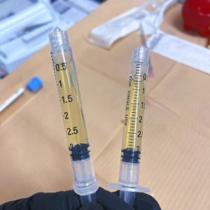Two syringes held upright, each partly filled with yellow fluid on a lab bench.
