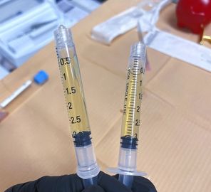 Two syringes filled with yellow liquid held in gloved hands on a lab bench