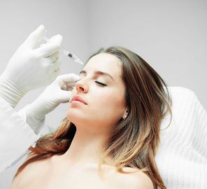 Woman receiving a cosmetic injection near her eye while reclining in a white clinical chair