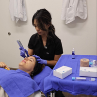Esthetician applying a treatment to a client lying on a spa bed with blue towels and supplies nearby
