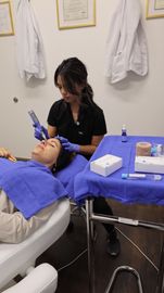Esthetician performing a facial treatment on a client in a spa room with towels and supplies nearby
