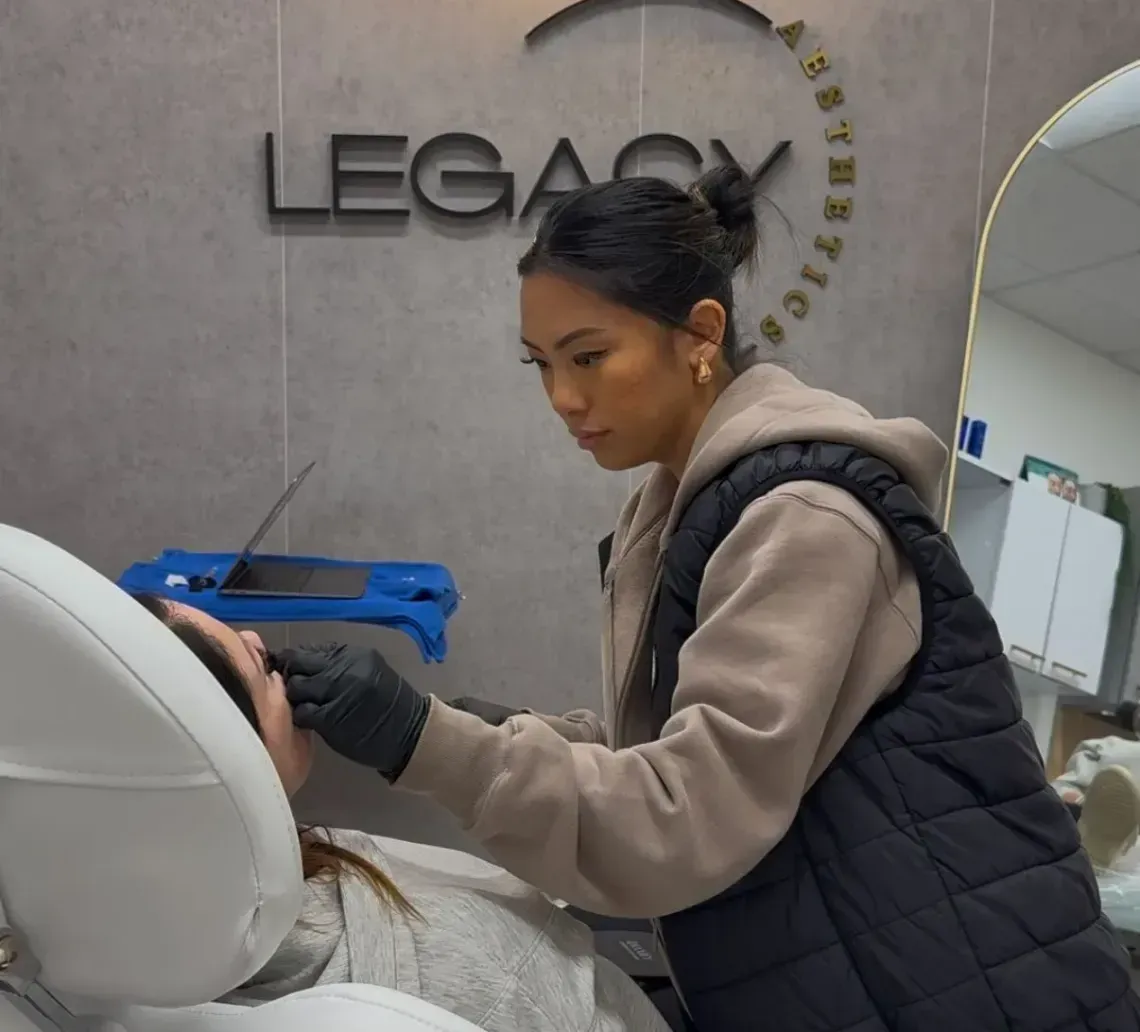 Person cleaning a white salon chair in a modern salon with a “LEGACY” sign on the wall