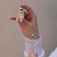 Hand holding a small medication vial and syringe, preparing an injection