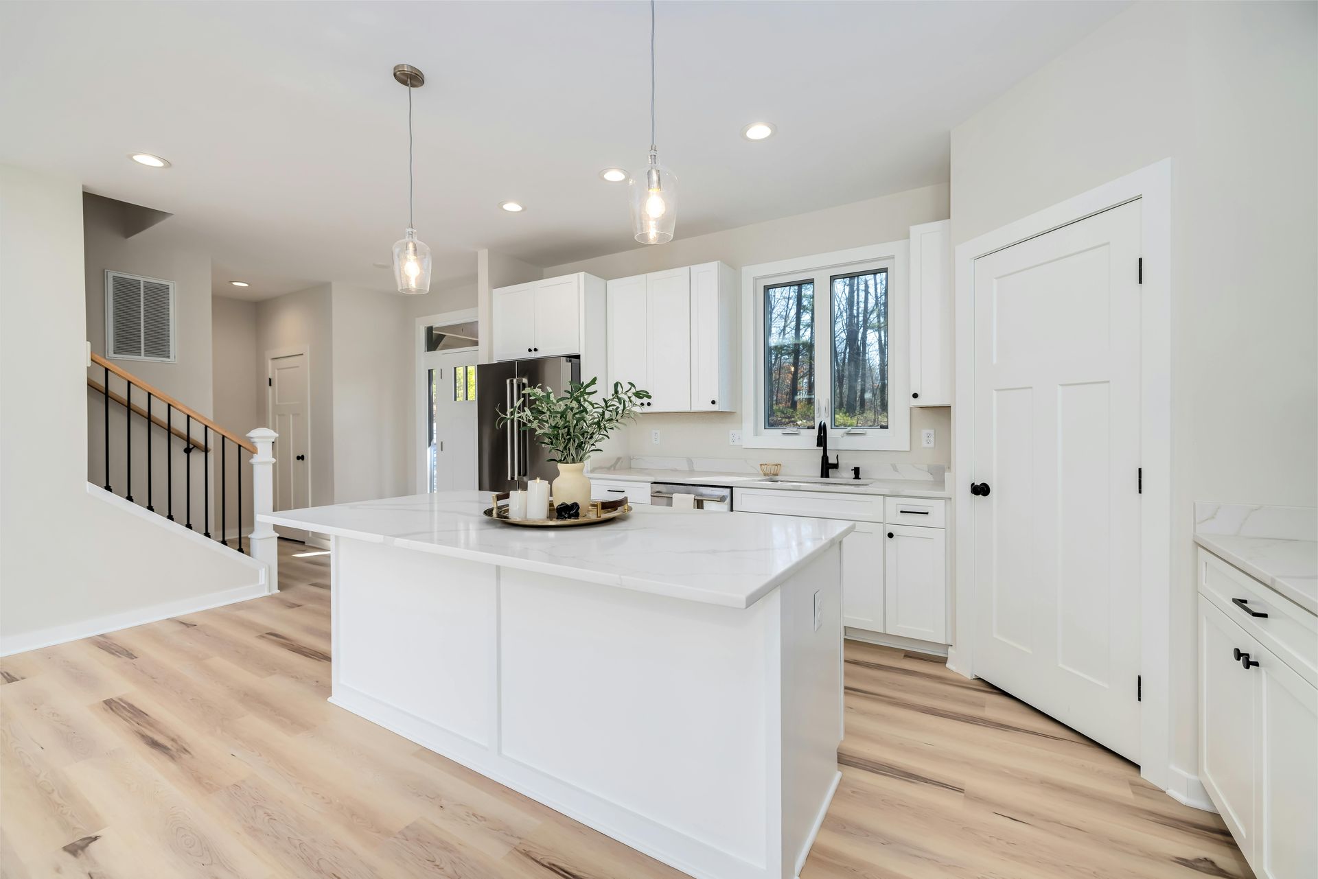 Bright modern kitchen with white cabinets, island, light wood floors, and staircase in the background
