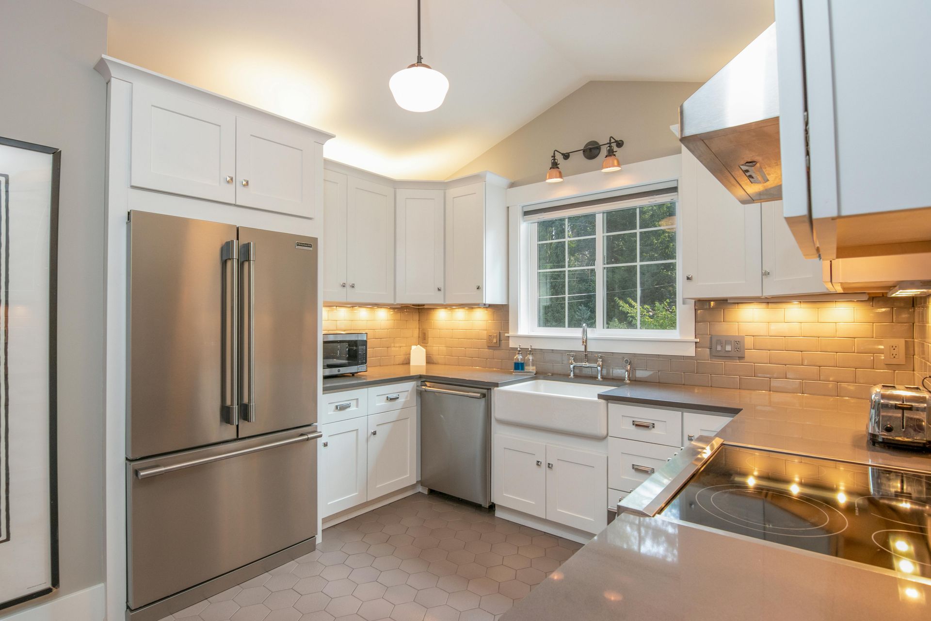 Bright white kitchen with stainless steel appliances, window over sink, and warm under-cabinet lighting.
