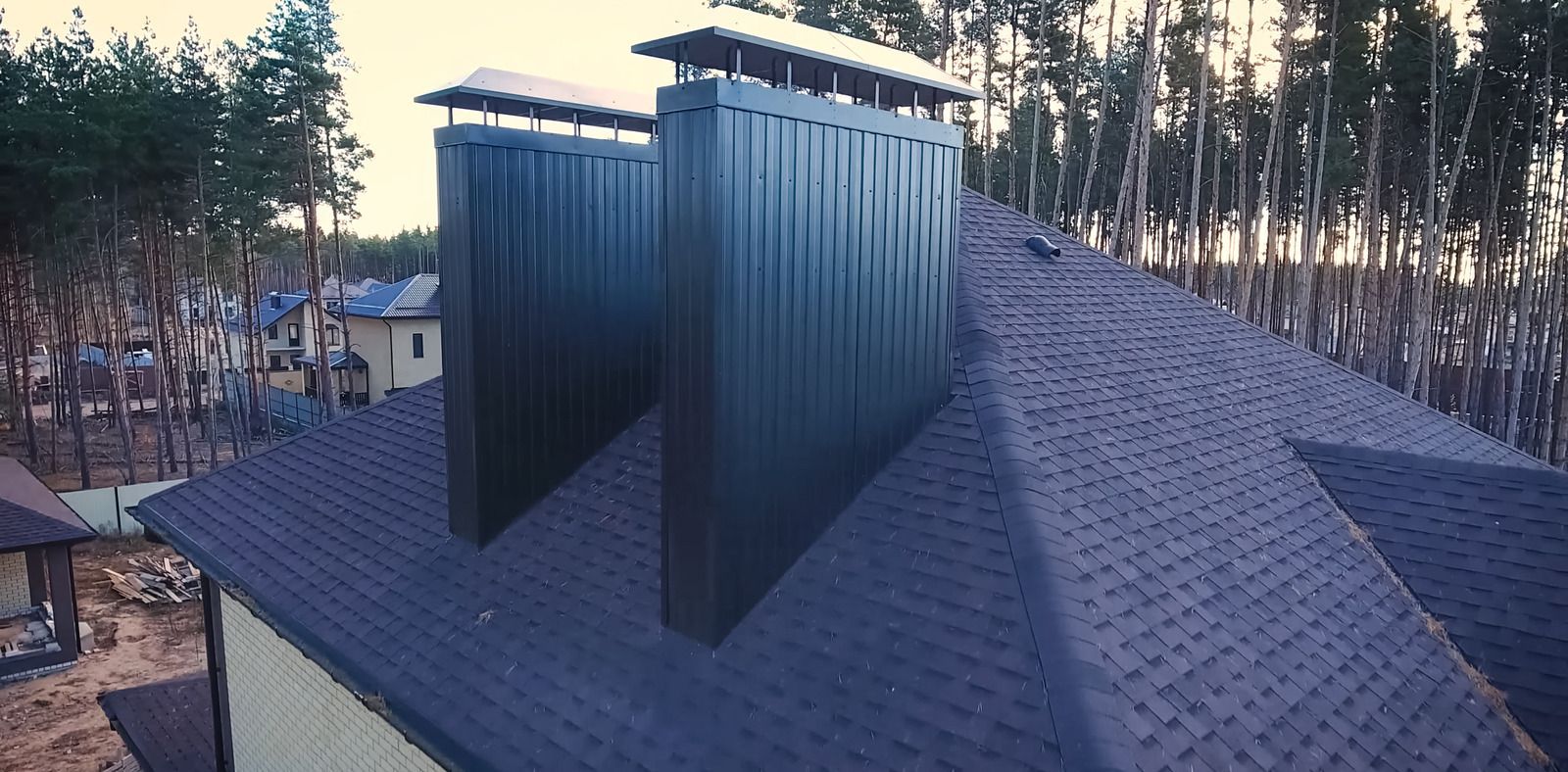 Metal roof vents on a shingled rooftop at dusk, with trees in the background.