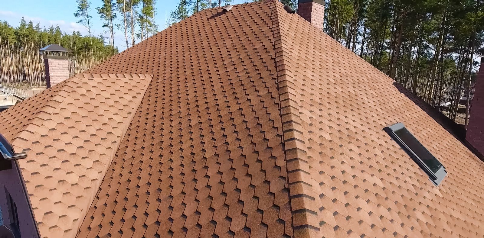Brown shingled roof with solar vent panels, surrounded by trees under a clear sky