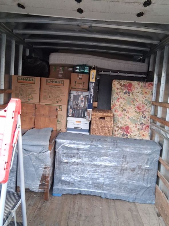 Cargo van packed with stacked boxes, wrapped pallets, and floral-patterned paneling inside.