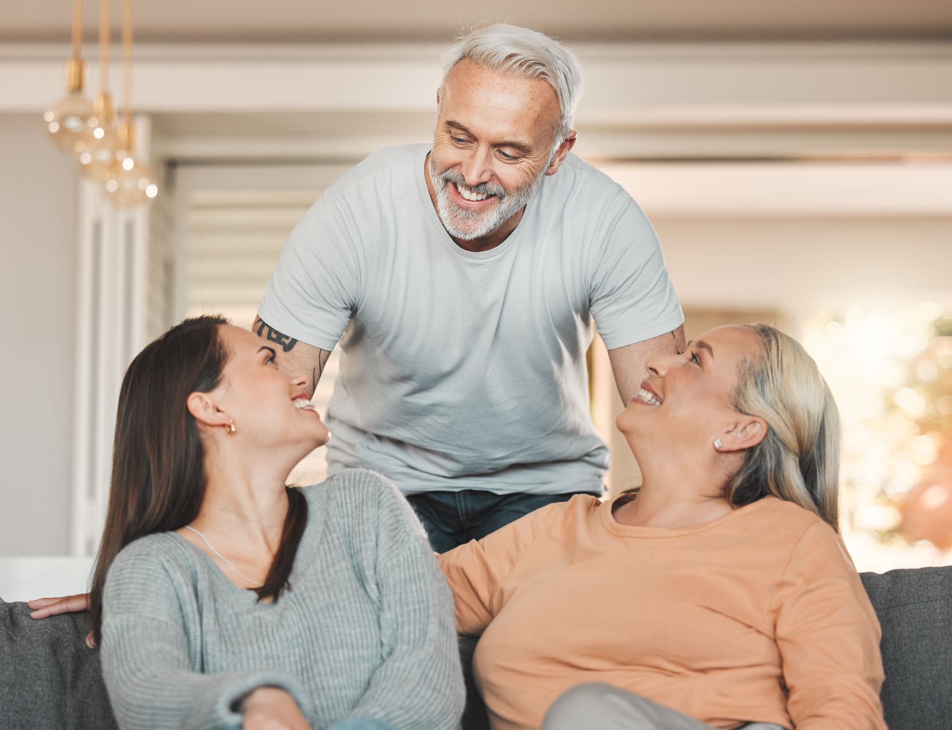 Three adults smiling and chatting on a couch in a bright living room