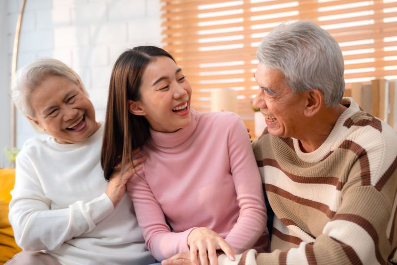 Three people smiling and chatting on a couch in a bright living room