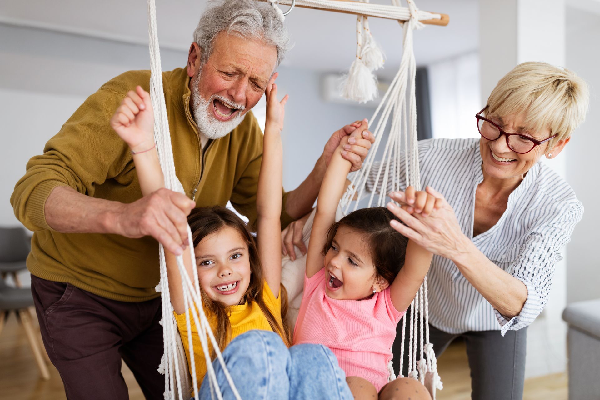 Family playing together on a white rope swing indoors, smiling and laughing