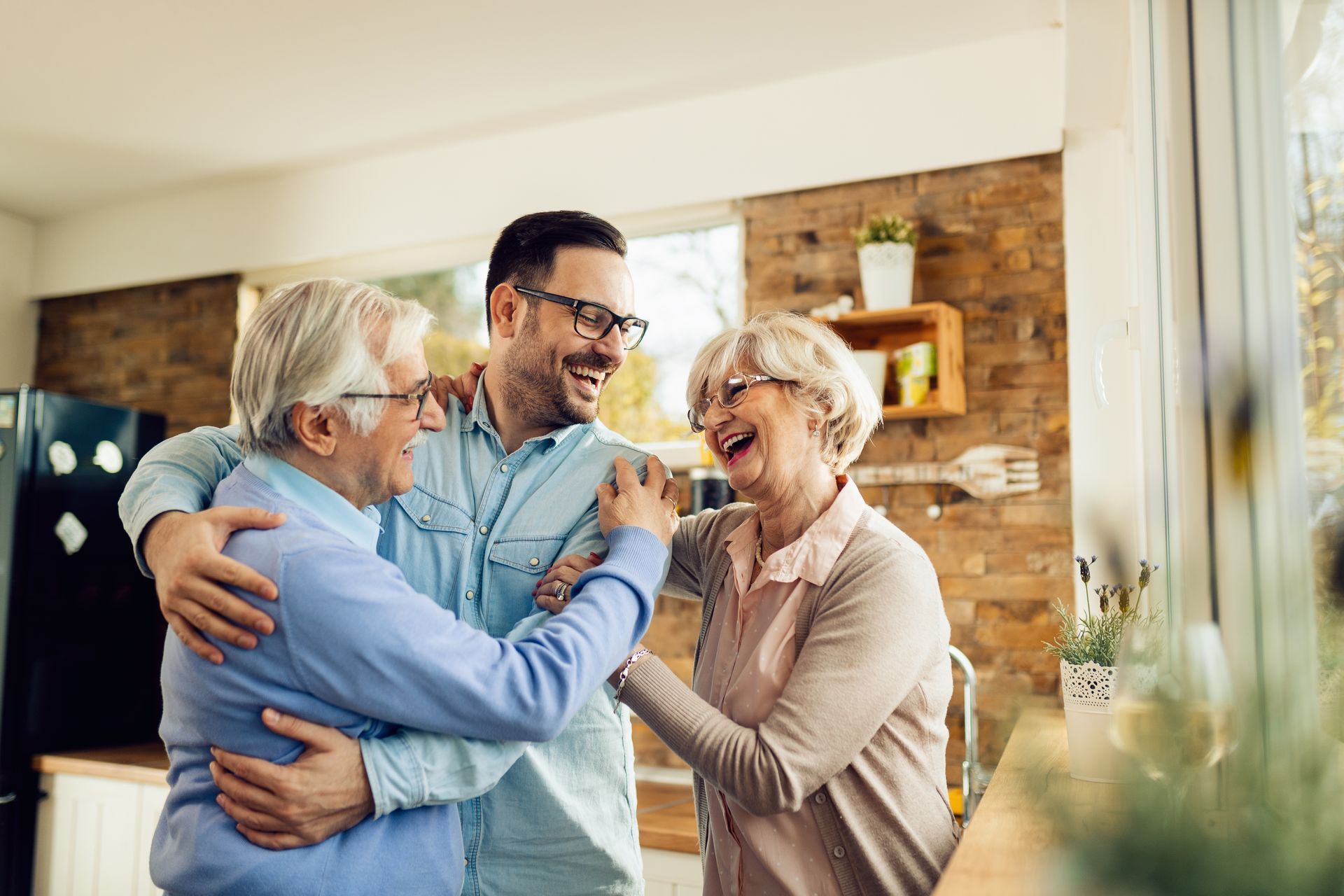Three people smiling and hugging in a bright home with a brick wall backdrop