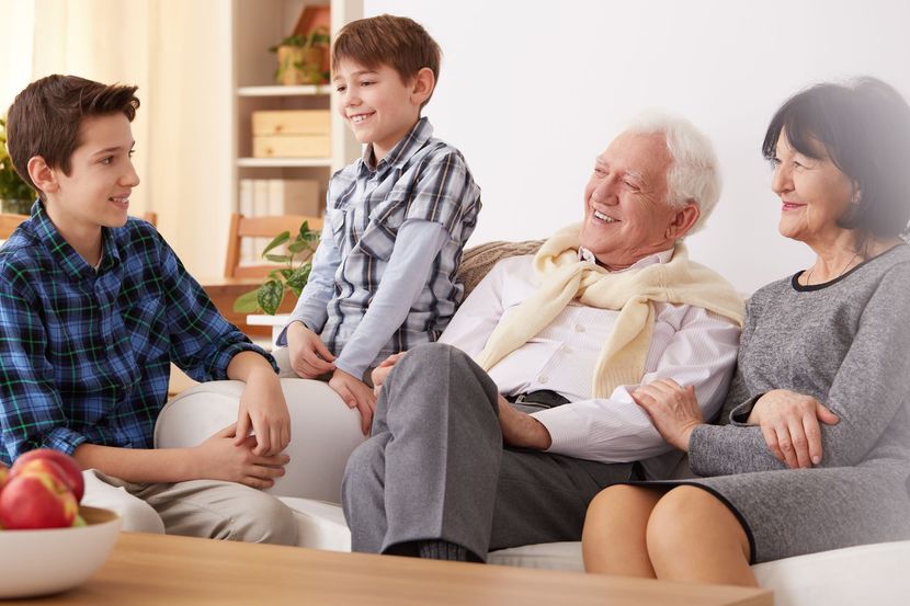 Four people sit together on a couch, smiling in a bright living room.