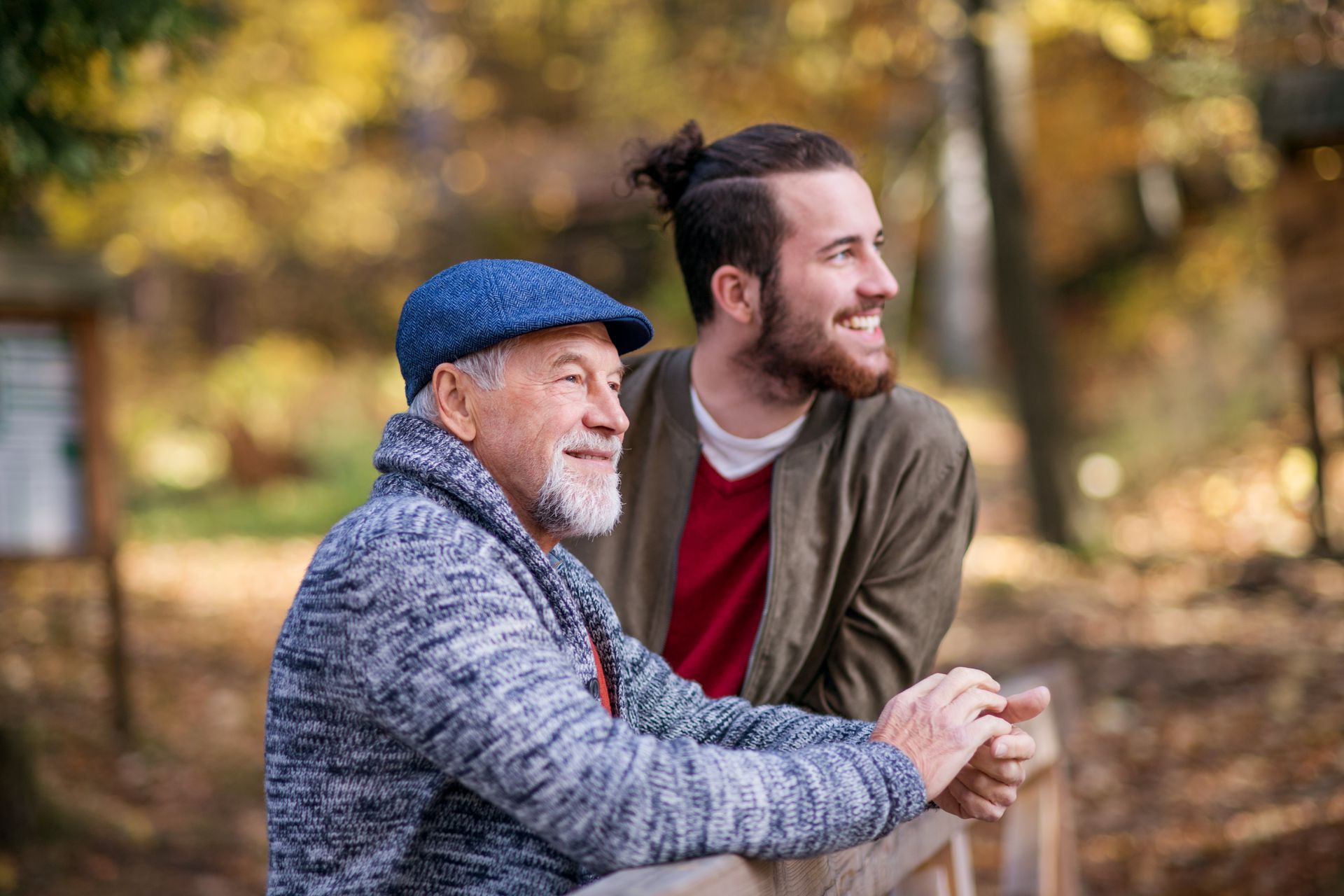 Two people smiling outdoors in autumn, leaning on a wooden railing.