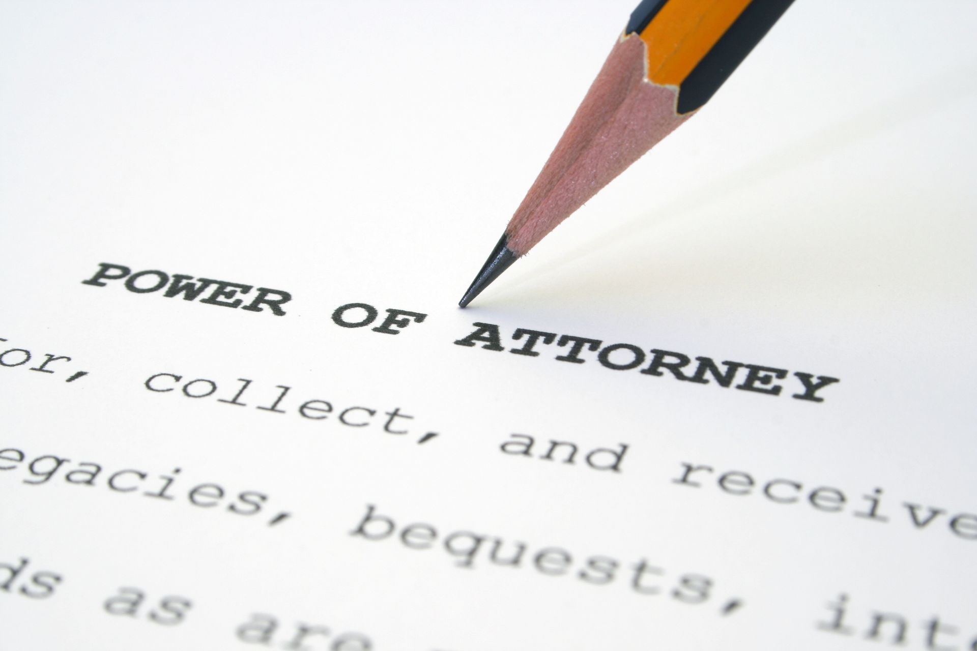 A pencil is writing the word power of attorney on a piece of paper