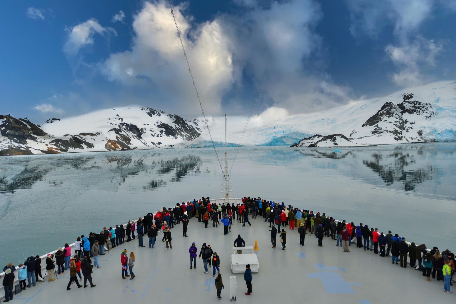 Crowd gathered on a snowy glacier beneath blue sky and clouds, with mountains in the background