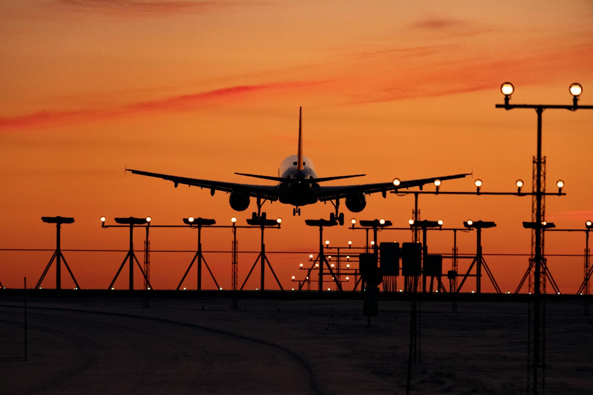 Airplane landing at sunset behind airport fencing and runway lights