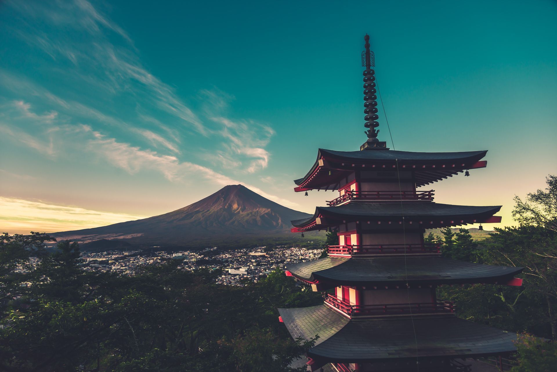 Pagoda silhouetted at sunset with Mount Fuji in the background and a glowing city below