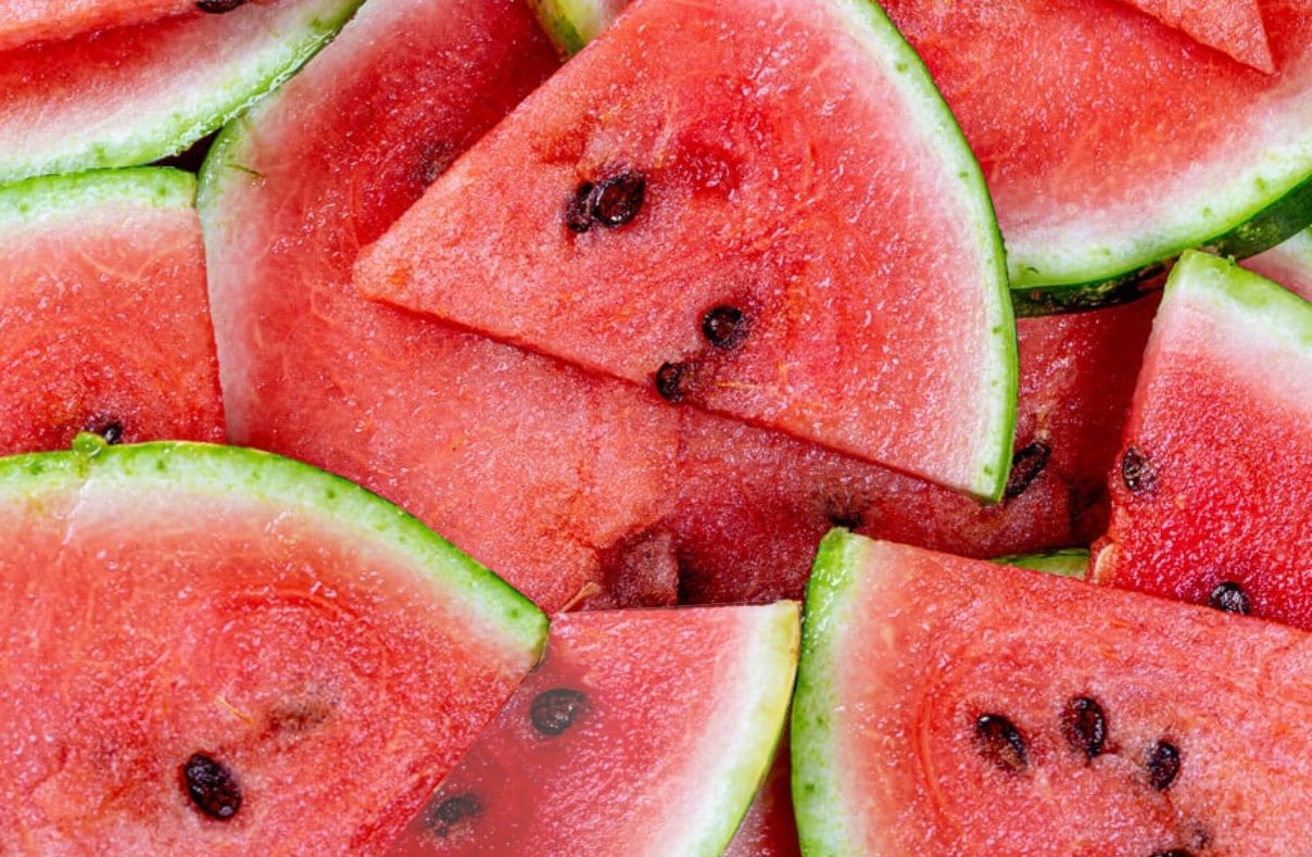 Slices of watermelon with bright red flesh, green rinds, and black seeds, tightly stacked together