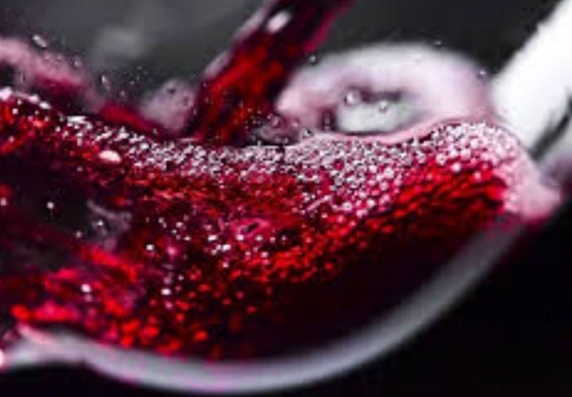 Close-up of red wine swirling in a glass, with bubbles and a dark background