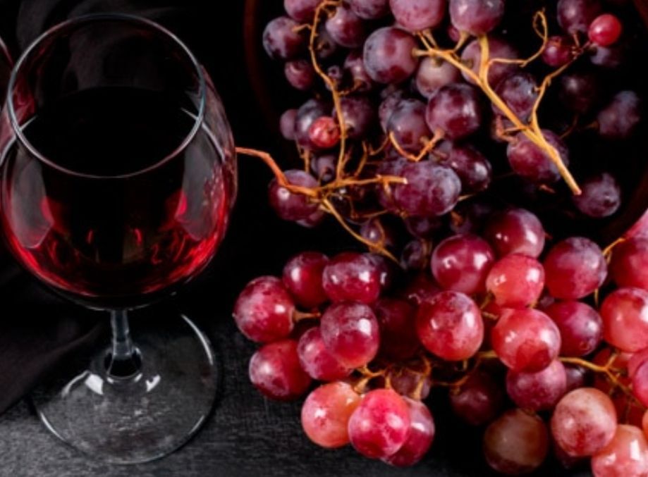 Glass of red wine beside red and purple grapes on a dark surface