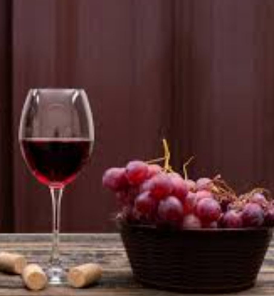 Wine glass and basket of red grapes on a wooden table against a dark background