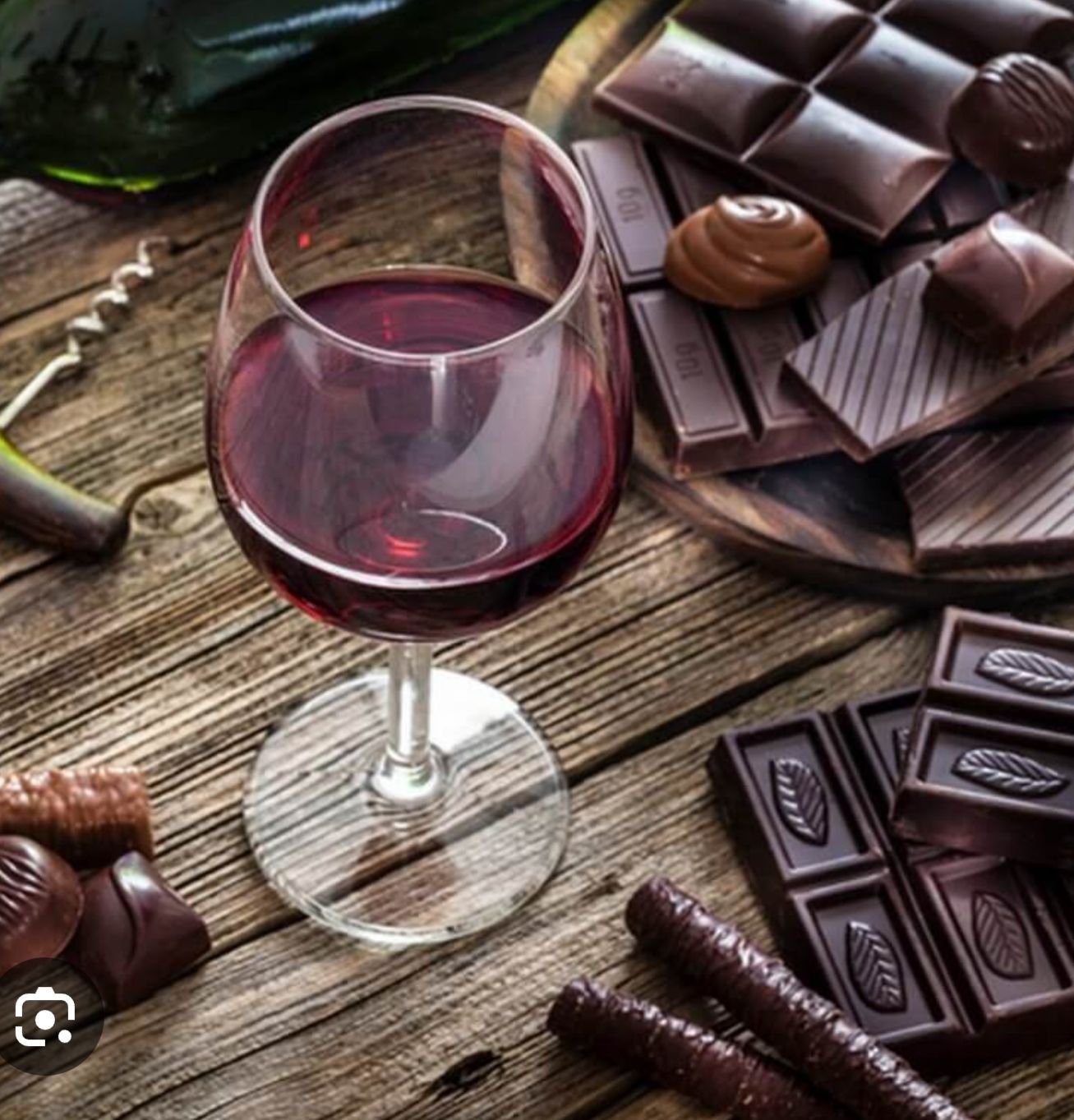 Glass of red wine beside assorted chocolate pieces on a rustic wooden table