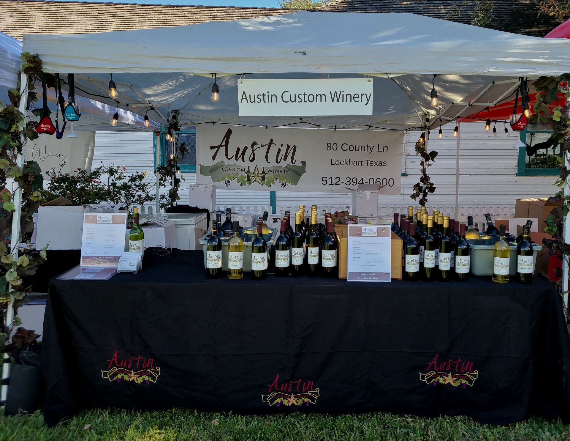 Austin Custom Winery booth with wine bottles displayed on a black tablecloth under a canopy.