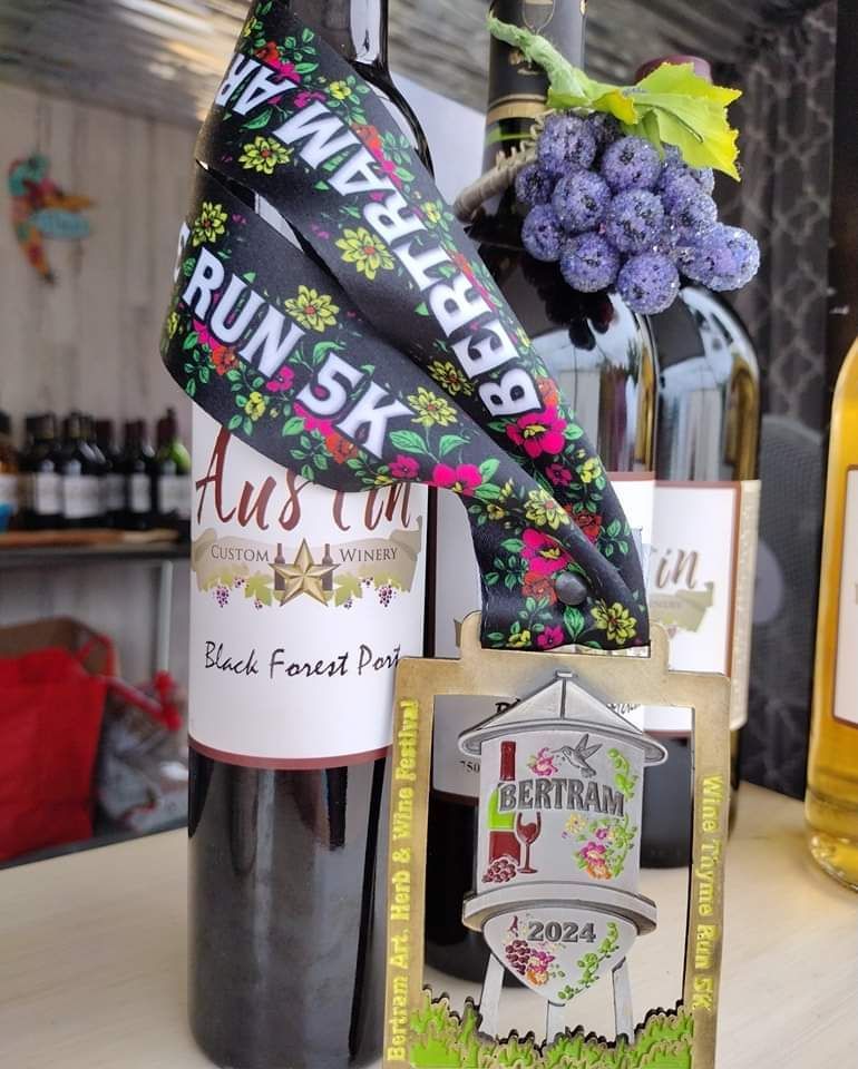 Wine bottle gift with floral decorations and “RUN 5K” ribbon, displayed beside a small sign on a table.