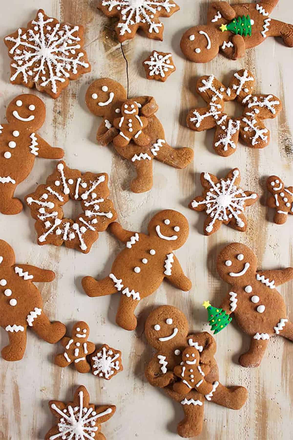 Gingerbread men, snowflakes, and stars decorated with white icing on a light wooden surface.
